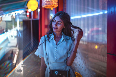 Portrait of smiling young woman standing in city at night