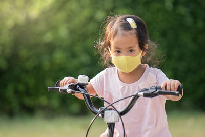 Little girl wearing anti pollution mask on her bike at park.