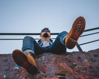 Low section of man relaxing against clear sky