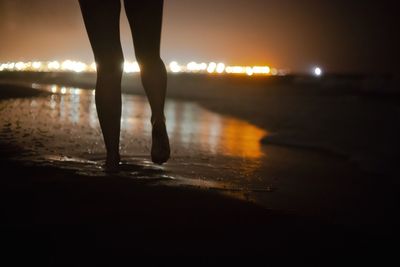 Low section of man standing on illuminated beach at night