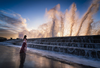 Woman looking at splashing water during sunset