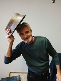 Portrait of smiling mature man holding container against wall