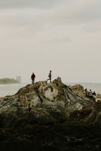 Men on rocky shore against sky