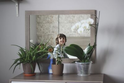 Portrait of boy with plants looking through window