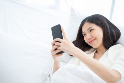 Young woman using mobile phone while sitting on bed