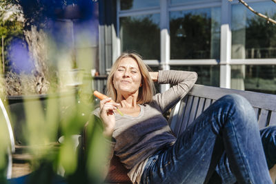 Woman relaxing on garden bench eating a carrot