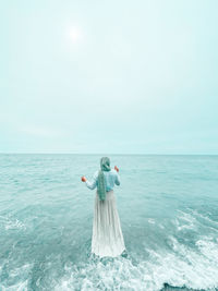 Rear view of woman standing at beach against sky