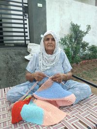 Portrait of senior woman knitting while sitting on bed outdoors