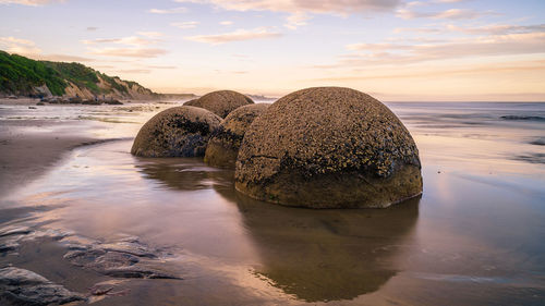 Rock formation on beach against sky during sunset