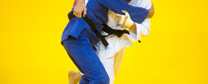 Midsection of people practicing martial arts against yellow background