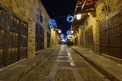 Illuminated road amidst buildings against sky at night