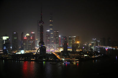 Illuminated cityscape by river at night