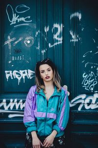 Portrait of smiling young woman standing against graffiti