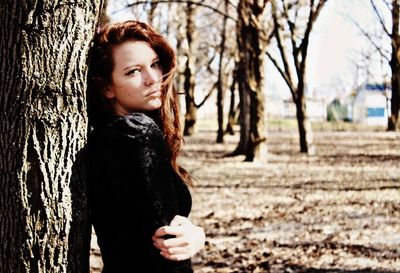 Side view of girl leaning against tree trunk