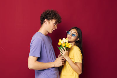 Young couple with bouquet standing against red background