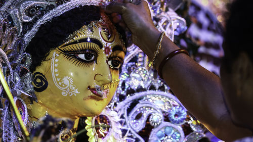 Cropped image of pundit applying sindoor to durga statue during durga puja festival