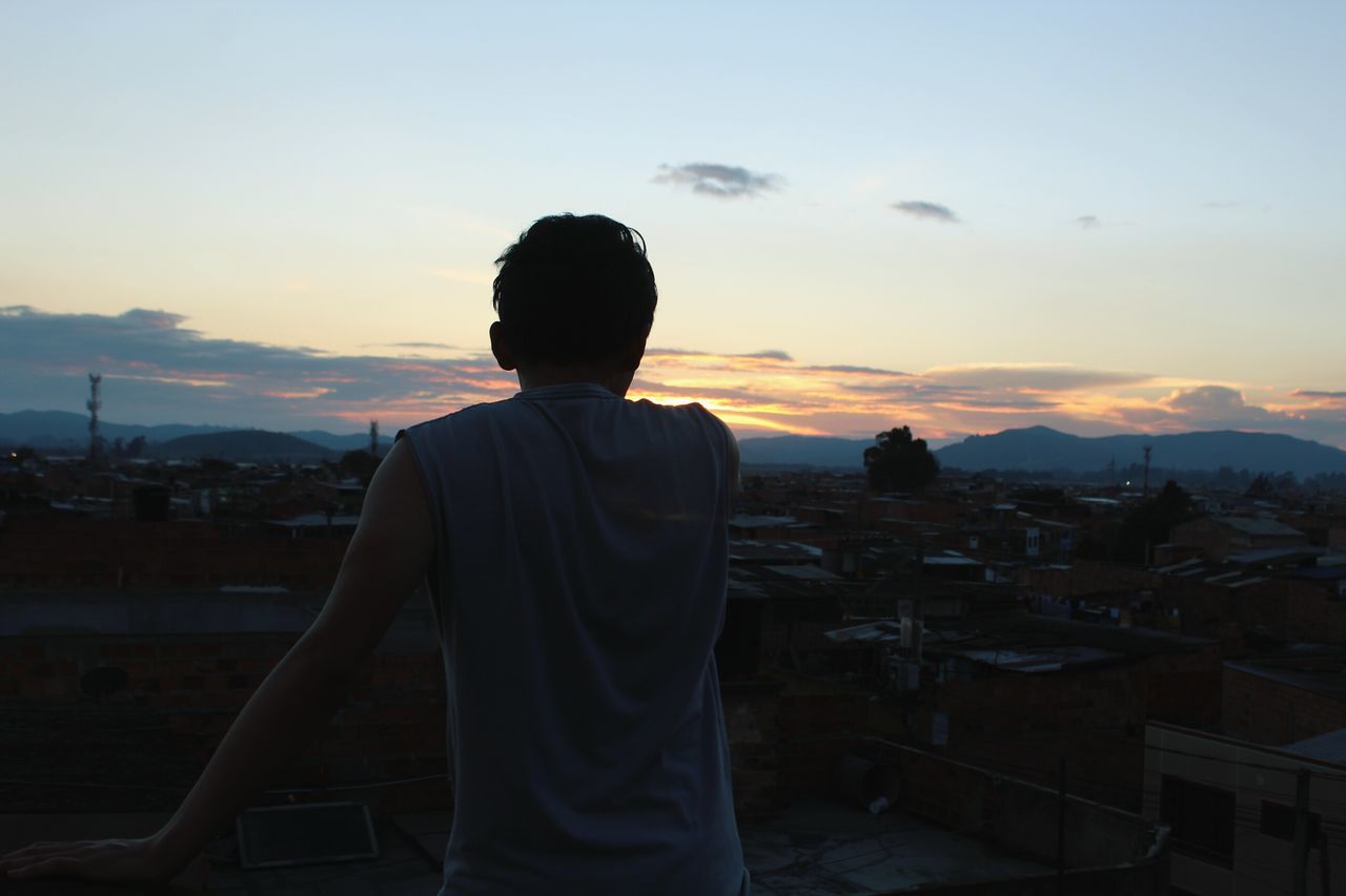 REAR VIEW OF MAN STANDING AGAINST CITYSCAPE