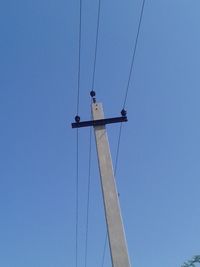 Low angle view of bird perching on cable against clear blue sky