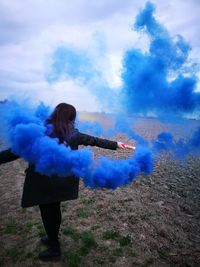 Rear view of woman holding distress flare on field