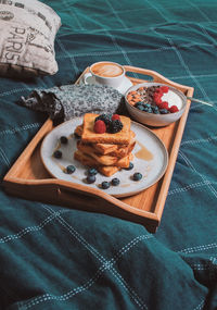 Breakfast in bed from above, yogurt bowl with berries and nuts, french toasts, coffee cup on plate