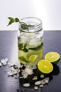 Close-up of mojito in glass jar by lime and ice on table