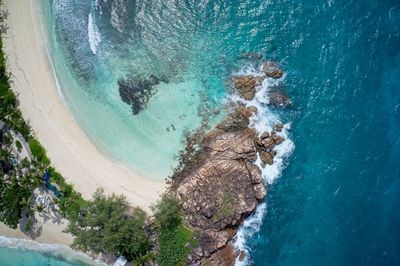 Drone field of view of waves crashing into rocky peninsula in praslin, seychelles.