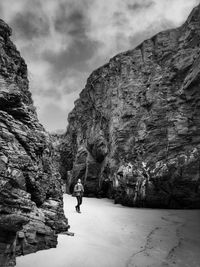 Man walking on rock by mountain against sky