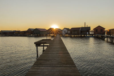 Pier over sea and houses against sky during sunset