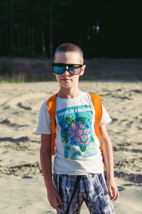 A seven-year-old boy in shorts, a t-shirt and sunglasses stands on a sandy glade