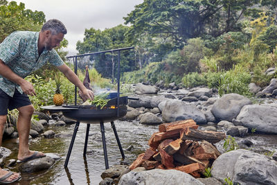 Chef cooking over open flame at campsite kitchen near stream