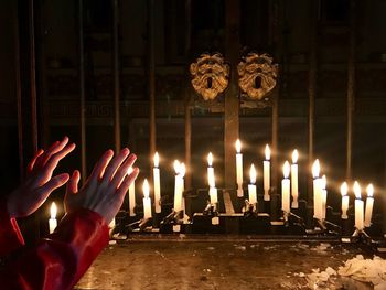 Cropped hands gesturing towards lit candles