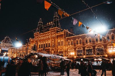 People at illuminated market stall against sky at night