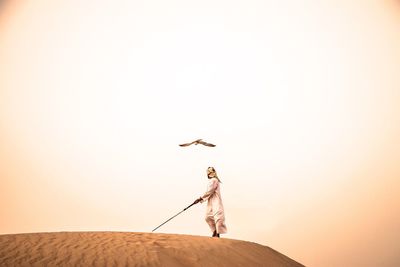 Low angle view of young man standing on sand at desert against sky during sunset