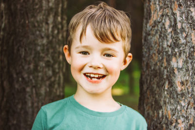 Portrait of cute boy looking away standing against tree trunk