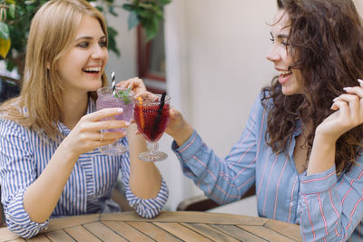 Cheerful young friends toasting drinks on table at restaurant