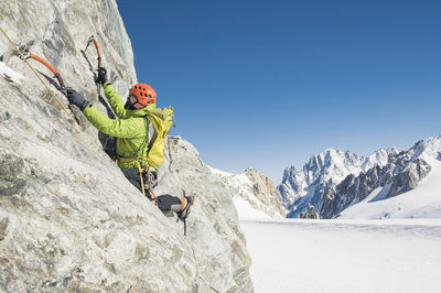 Male hiker climbing mountain against clear blue sky during winter