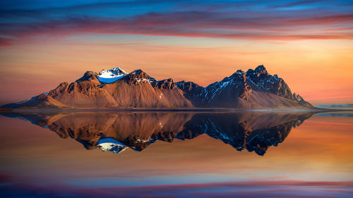 Scenic view of lake by snowcapped mountains against sky during sunset