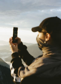 Portrait of woman photographing through smart phone against sky