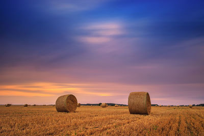 Hay bales on field against sky during sunset