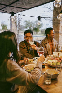 Smiling young man holding wineglass sitting with friends at dining table in patio