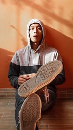 Portrait of young man sitting against wall at home