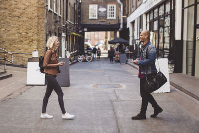 Full length side view of couple walking towards each other on road in city