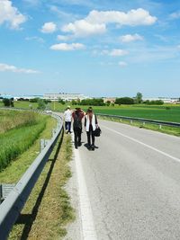 Rear view of people walking on road against sky