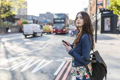 Woman with smart phone waiting at roadside in city