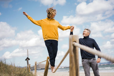 Mature man holding hand of woman assisting her walking on rope at beach