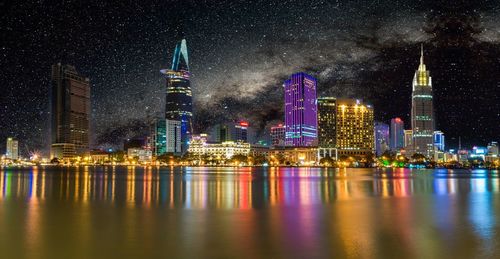 Illuminated skyscrapers in city with reflection against stars in sky