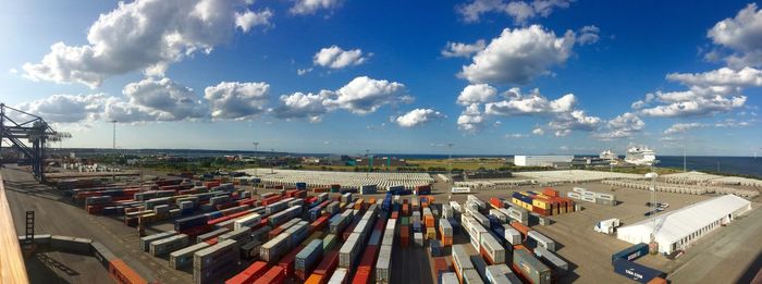 Cargo containers at commercial dock against cloudy sky