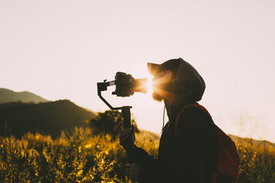 Side view of young man photographing from camera against clear sky