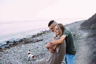 Happy couple with favourite pet. young man and woman have walk near sea.