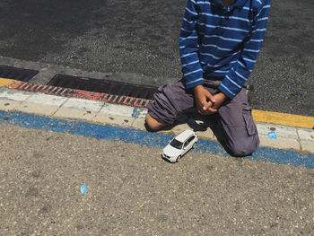 Low section of boy kneeling by toy car on footpath